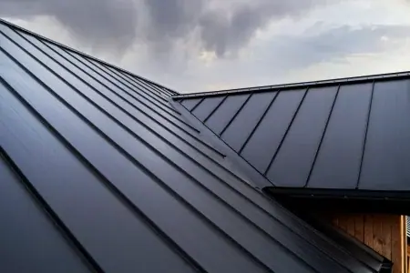 Close-up view of a modern dark metal roof with standing seam panels, set against a cloudy sky background.