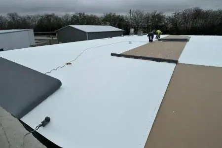 Two workers, including a roofer in Winter Haven, install large white roofing sheets on a flat commercial roof under cloudy skies; tools and materials are visible on the roof.