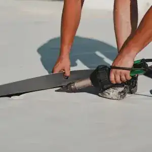 Two people install TPO and modified bitumen roofing using a hot air welding tool, with their hands and feet visible working on a flat, white surface.