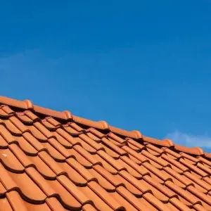 Close-up of a red clay tile roof under a clear blue sky, showcasing expert tile roof installation and the durability of clay and concrete tile roofing.