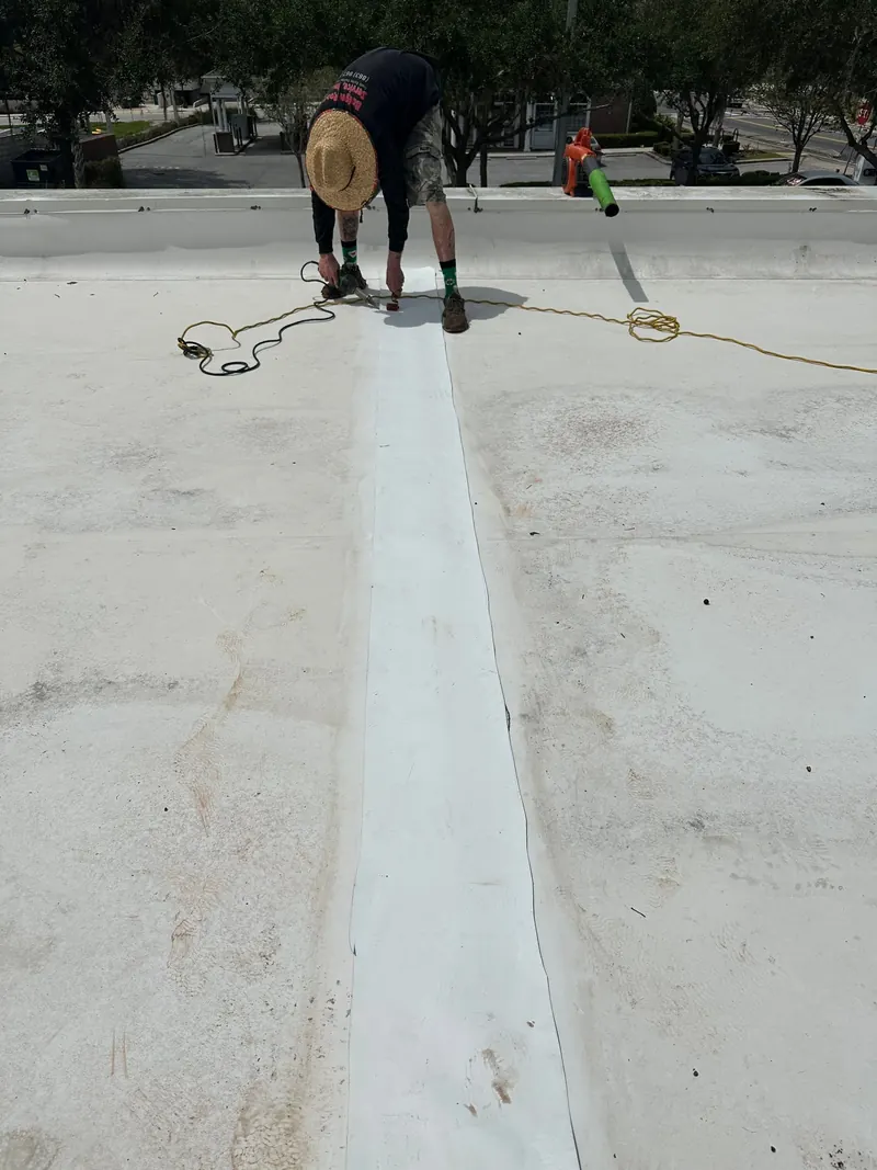 Roofer working along a new seam strip on a white commercial flat roof