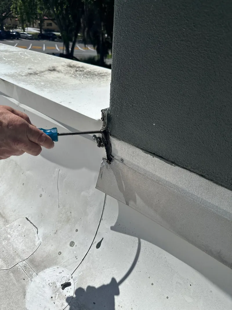 Roofer checking with a screwdriver where wall flashing has pulled away from a stucco wall on a flat roof