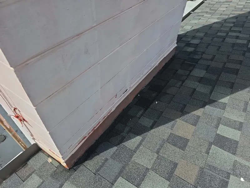 Painted wall meeting a shingle roof, with worn sealant and rust stains along the wall flashing