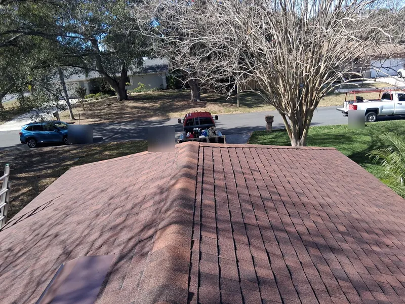 Ridge of a red-brown shingle roof on a Lakeland home, with a work truck in the street below