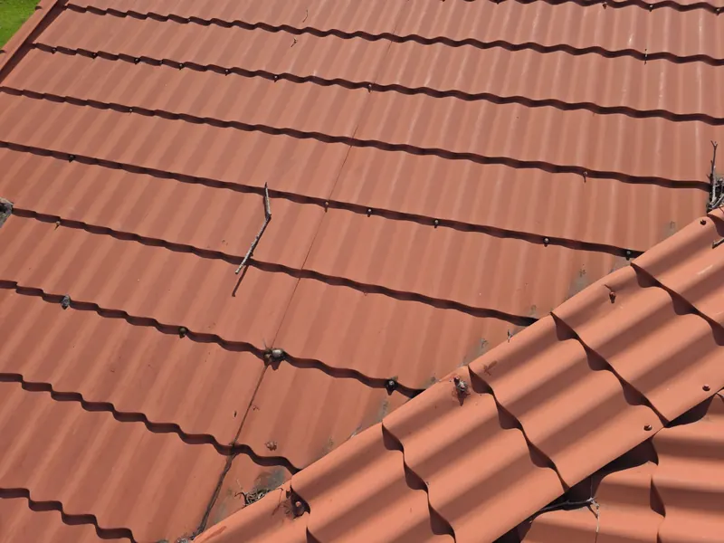 Red tile-profile metal roof panels meeting a hip cap