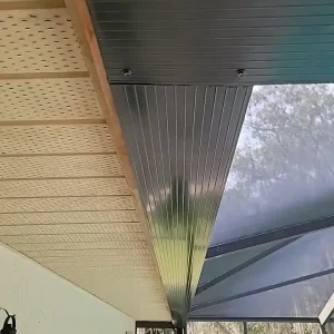 Close-up view of a covered patio roof with metal paneling by Budget Roofing Service Inc, adjacent to a screened enclosure and outdoor light fixture—a quality touch from a trusted roofing company in Winter Haven.