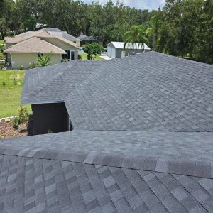 View of a house with a newly installed dark asphalt shingle roof by Budget Roofing Service Inc, surrounded by green grass, trees, and nearby houses—a testament to quality from a trusted roofing company in Winter Haven.