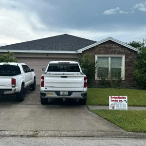 A one-story brick and siding house with two white trucks parked in the driveway and a "Budget Roofing Service Inc." sign on the lawn, showcasing a trusted roofing company in Winter Haven.