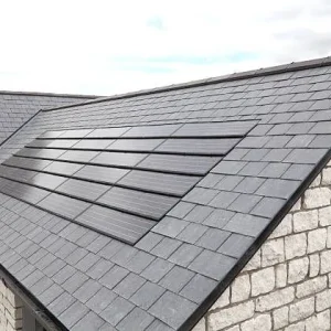 A sloped roof with gray slate tiles and integrated solar panels sits atop a stone building under a cloudy sky, showcasing modern low slope roofing systems designed for energy efficiency and durability.