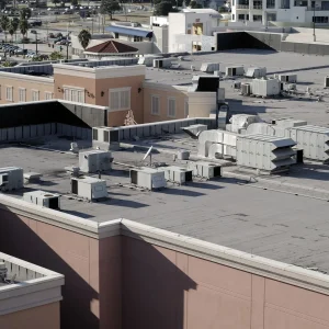 Flat commercial building rooftops featuring TPO and modified bitumen roofing with multiple HVAC units and ventilation ducts, surrounded by other structures, streets, and palm trees in the background.