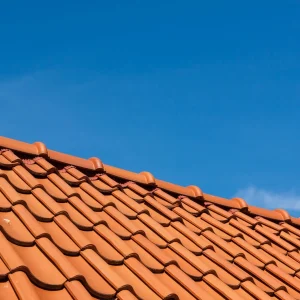 Close-up of a red clay tile roof under a clear blue sky, showcasing expert tile roof installation and the durability of clay and concrete tile roofing.