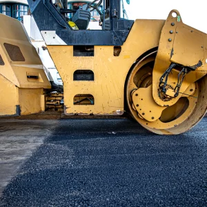 Close-up of a yellow road roller flattening fresh asphalt on a street during a road construction project.