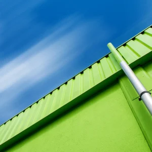 A green industrial building with a silver pipe and a blue sky with blurred clouds above.