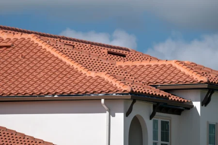 Close-up view of a house roof with red clay tiles, white exterior walls, arched windows, and blue sky with clouds—expertly maintained by Budget Roofing, a trusted roofing company in Winter Haven.