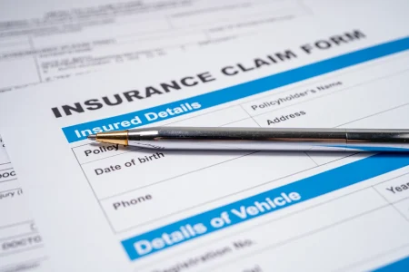 A silver pen rests on top of an insurance claim form, showing sections for insured details and vehicle information—perhaps the first step in filing a claim with Budget Roofing, a trusted roofing company in Winter Haven.