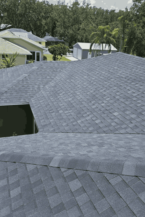 A view from above showing the dark grey shingled roof of a house in a suburban neighborhood with green lawns and trees, highlighting the quality work by a leading roofing company in Winter Haven.