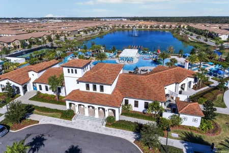 Aerial view of a residential community with a central clubhouse, outdoor pool, palm trees, and a large lake with a fountain surrounded by homes serviced by trusted roofers in Davenport FL.